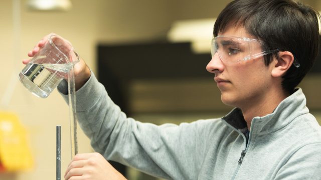 Chemistry student pouring liquid into test tube.