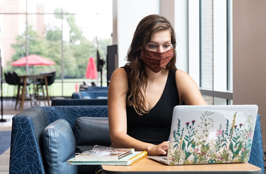 Young lady wearing a mask sits in front of a laptop