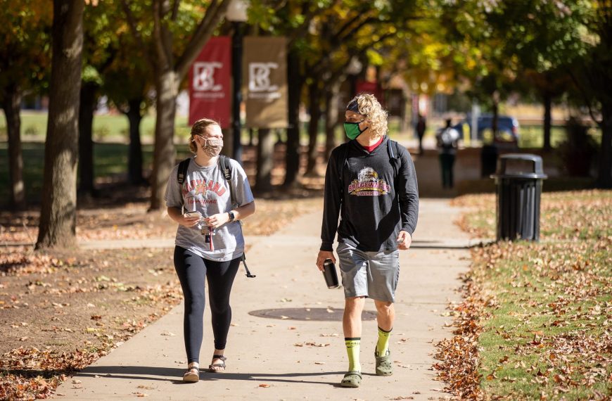 A female and male student walk on Bridewater's campus wearing masks