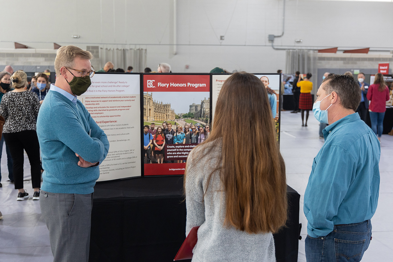 Woman and man standing in front of another man and presentation board about the Flory Honors Program.