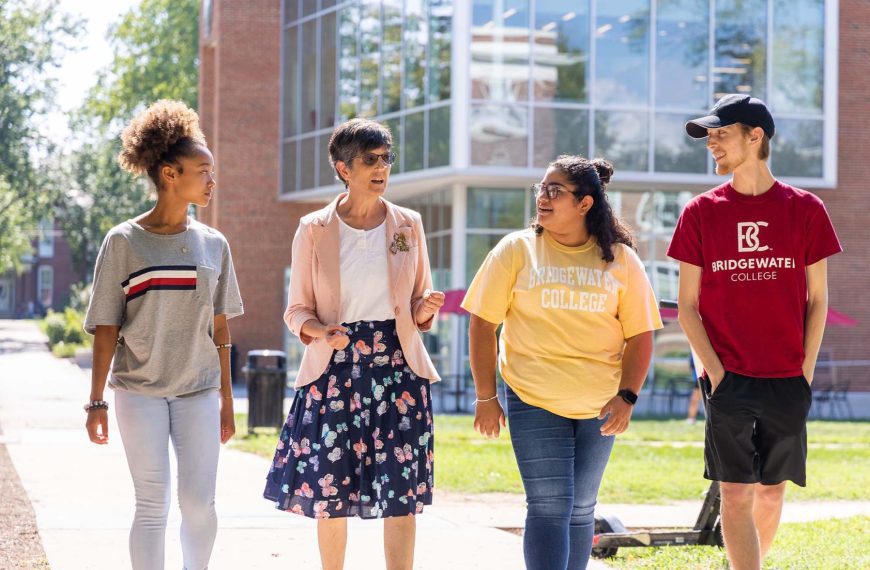 3 students walk alongside a professor on a sunny day