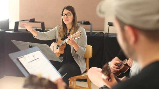 Music professor sitting in chair with guitar directing the class