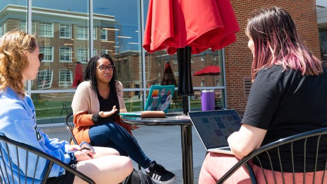 Students sitting at a table with an umbrella talking outside the Forrer Learning Commons