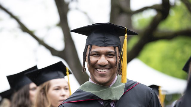 student smiling wearing cap and gown at commencement