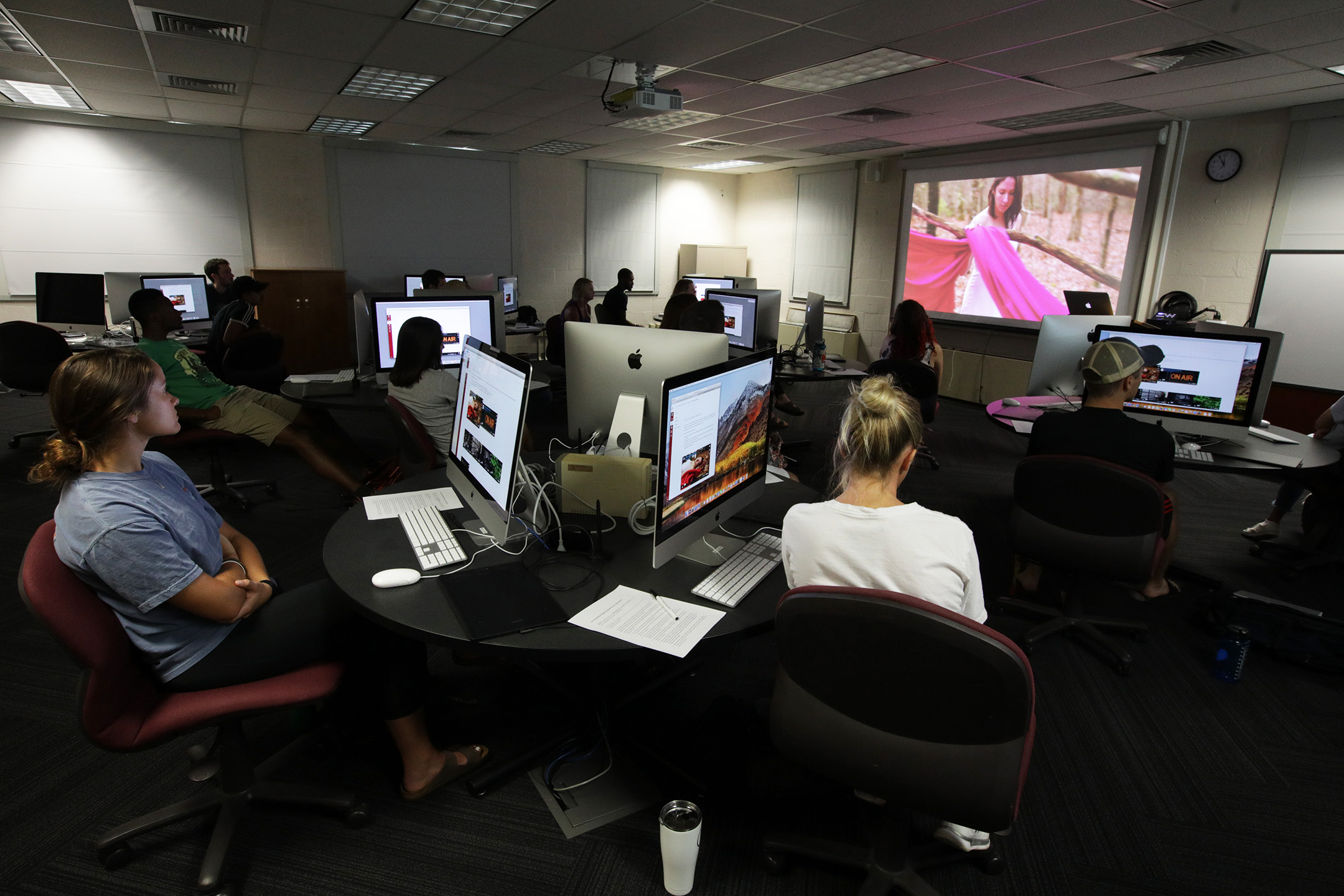 Students in a digital media classroom with mac computers and a projector