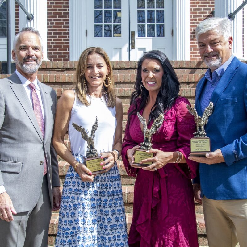 Two men and two women pose for a photo holding trophies and smiling.