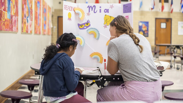 Student teacher sitting with an elementary school student in front of trifold presentation for a reading project