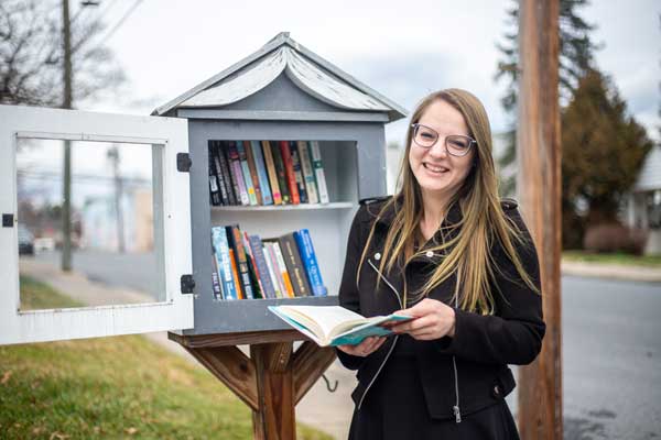Taylor Baugher stands in front of a Little Free Library.
