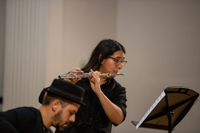 A woman playing the flute while looking at a music stand