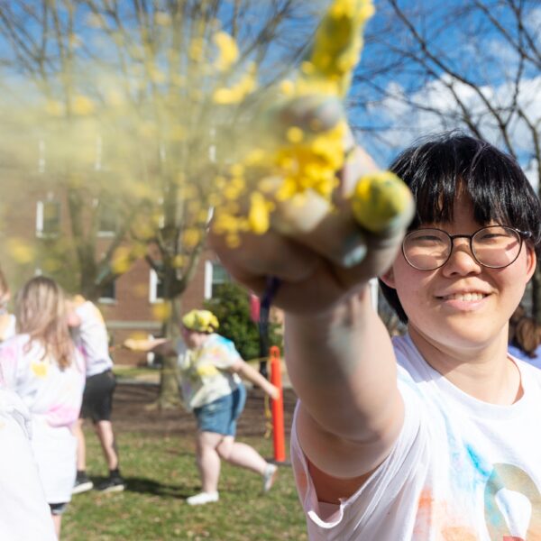 A student looks into the camera pointing upwards with yellow glitter falling off their hand.