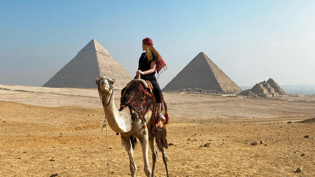 Student riding a camel in front of pyramids in Egypt