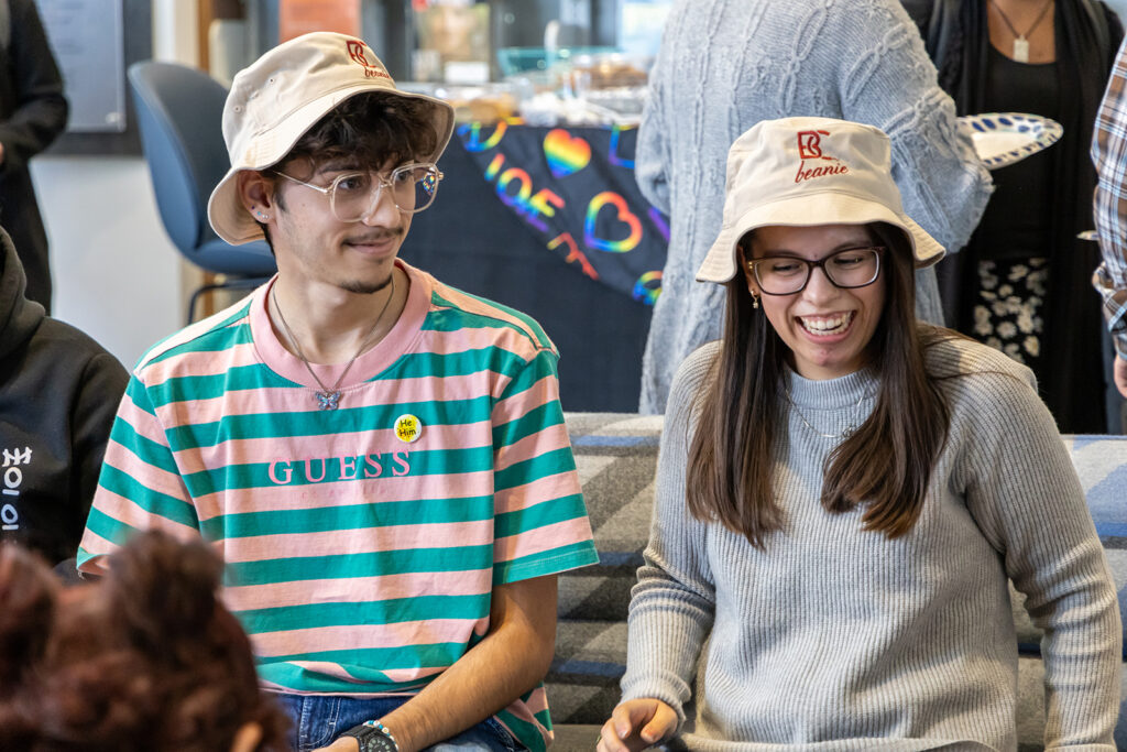 Two students with B-C floppy hats smiling sitting next to each other