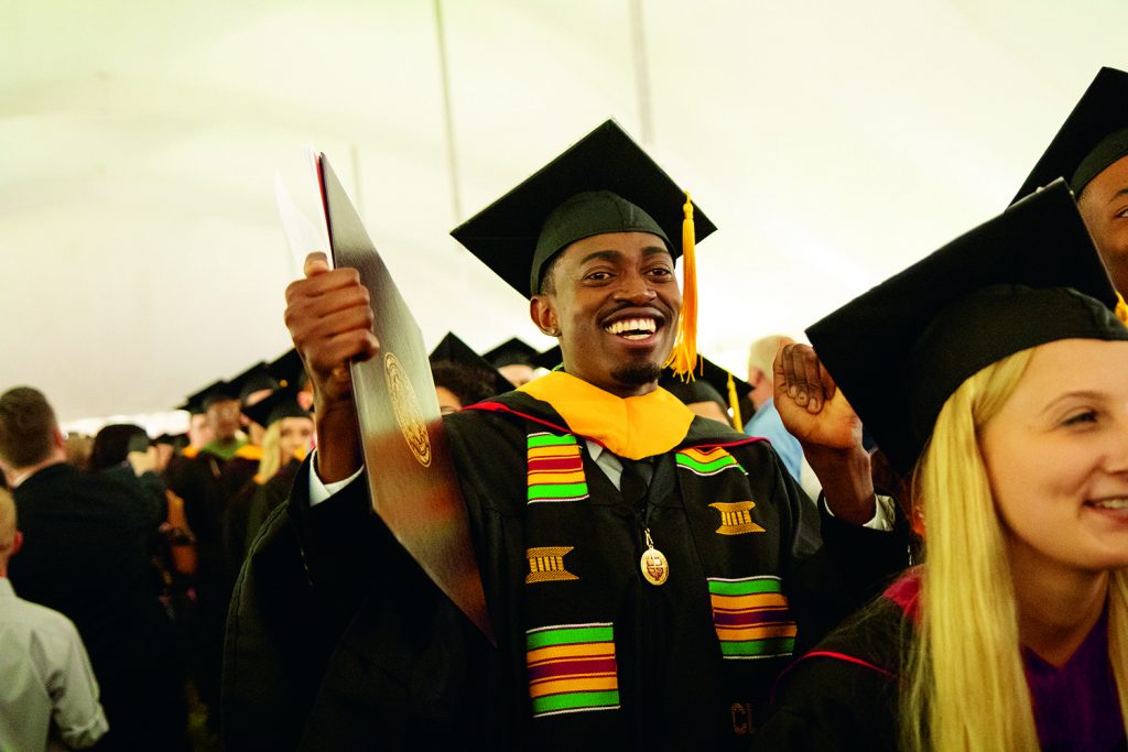 BC graduate at commencement holding up diploma in excitement