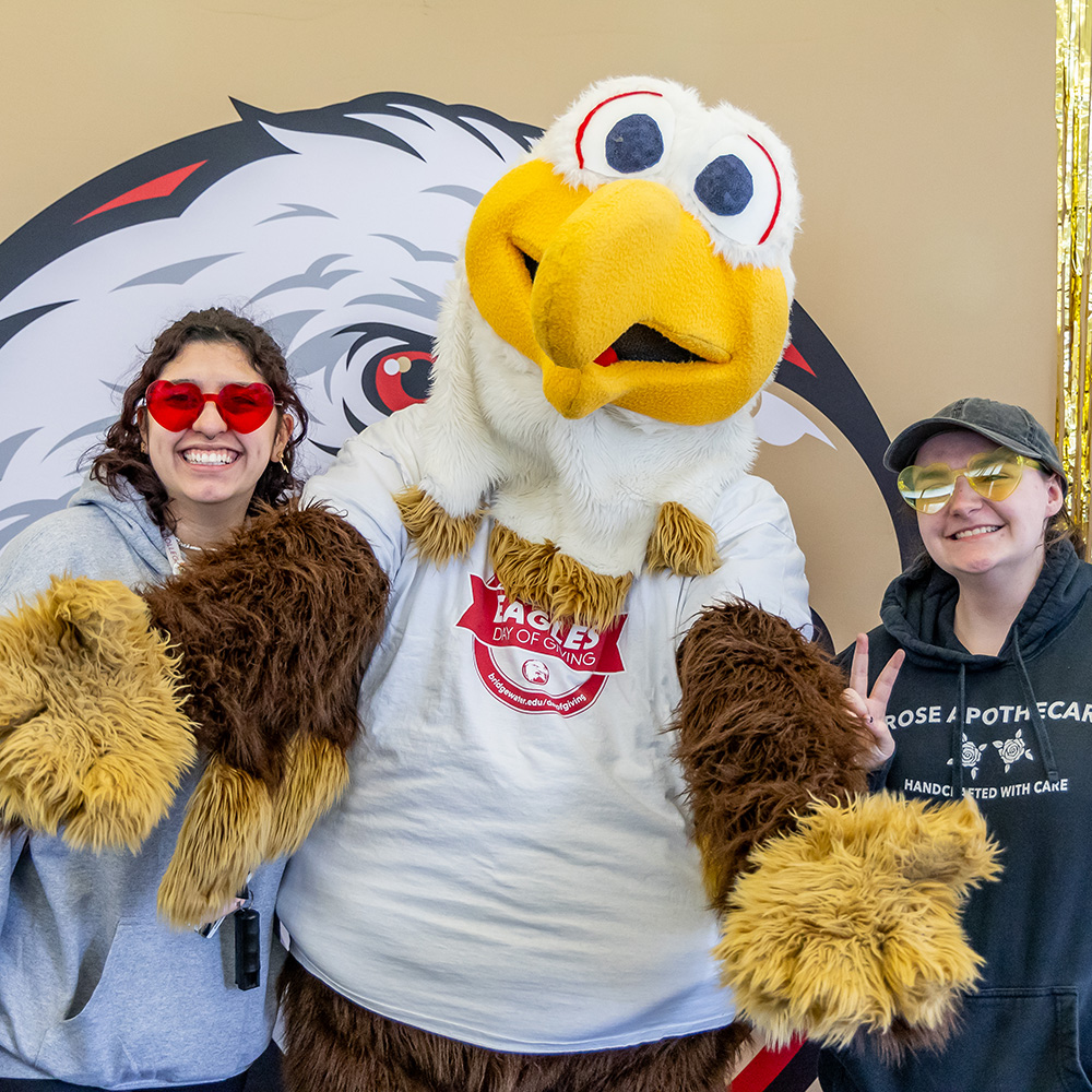 Mascot Ernie with arms outstretched and two student on either side of him