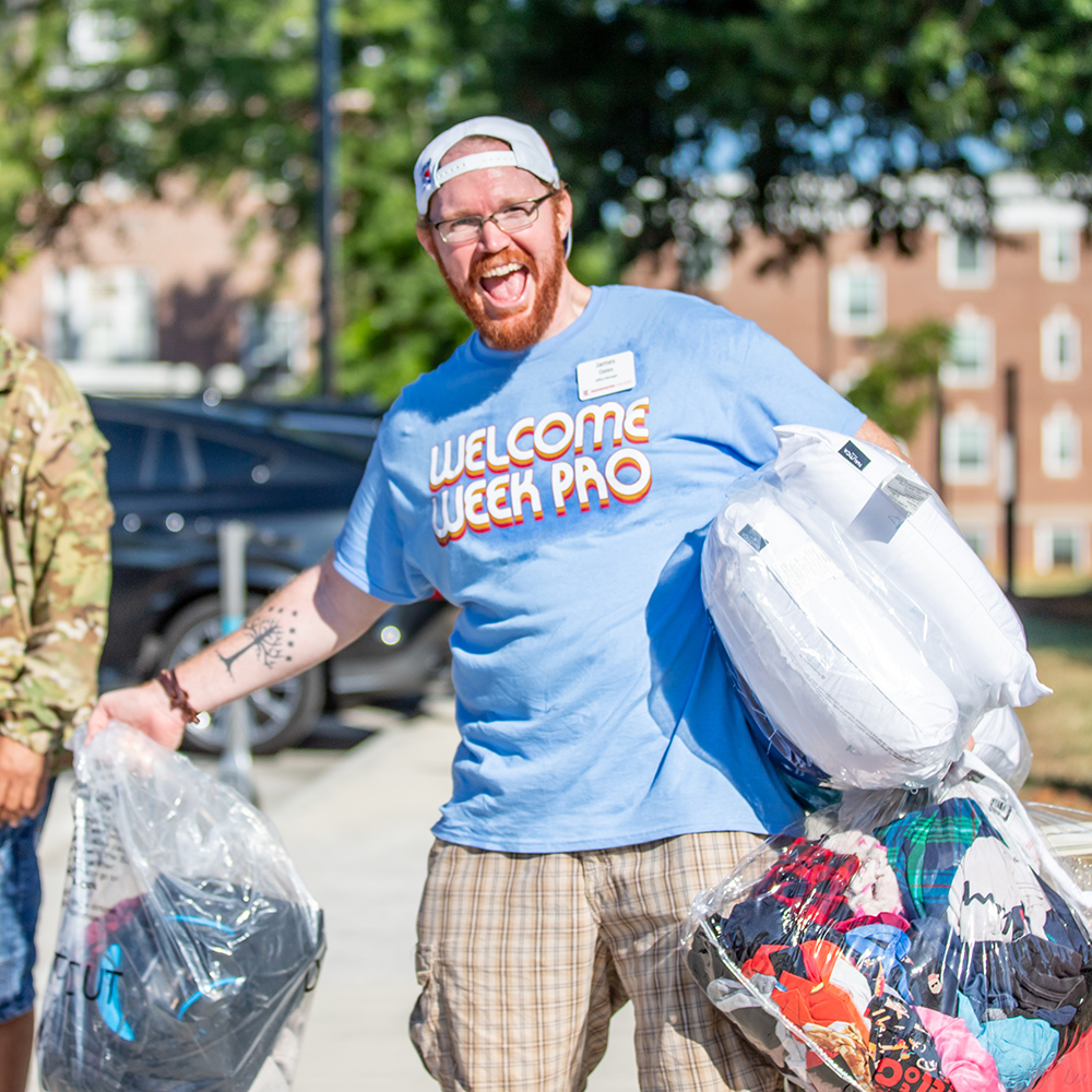 Man wearing Welcome Week Pro t-shirt while carrying three bags of clothes