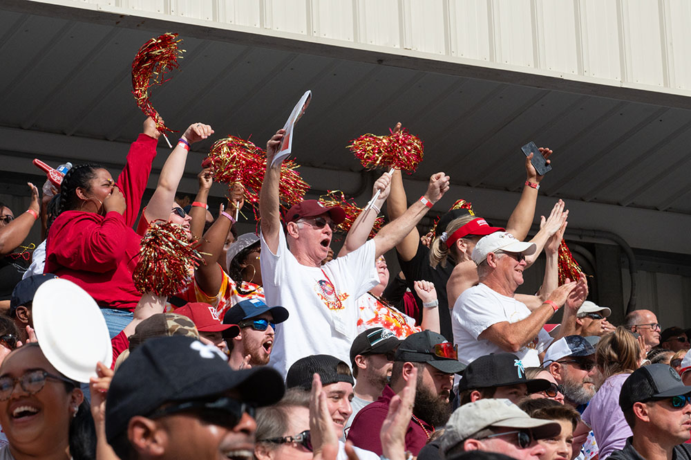 Group of fans standing up with raised hands cheering on the football team