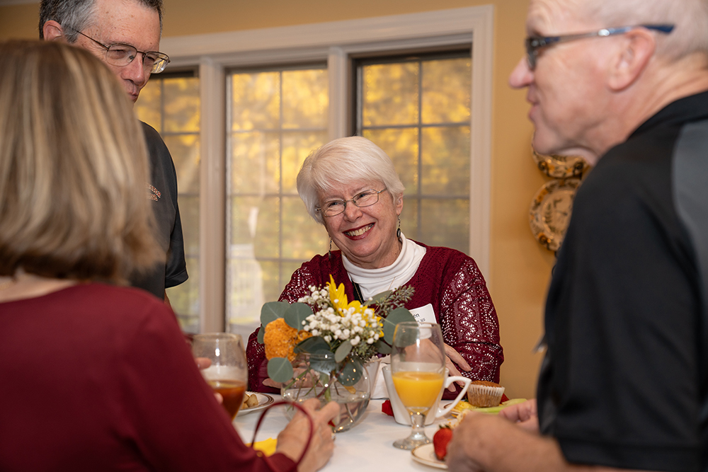 Older lady smiling while standing at a table with flowers in the middle