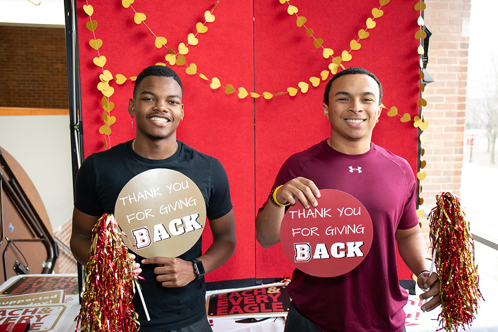 Two student holding up circular signs that say Thank you for giving back