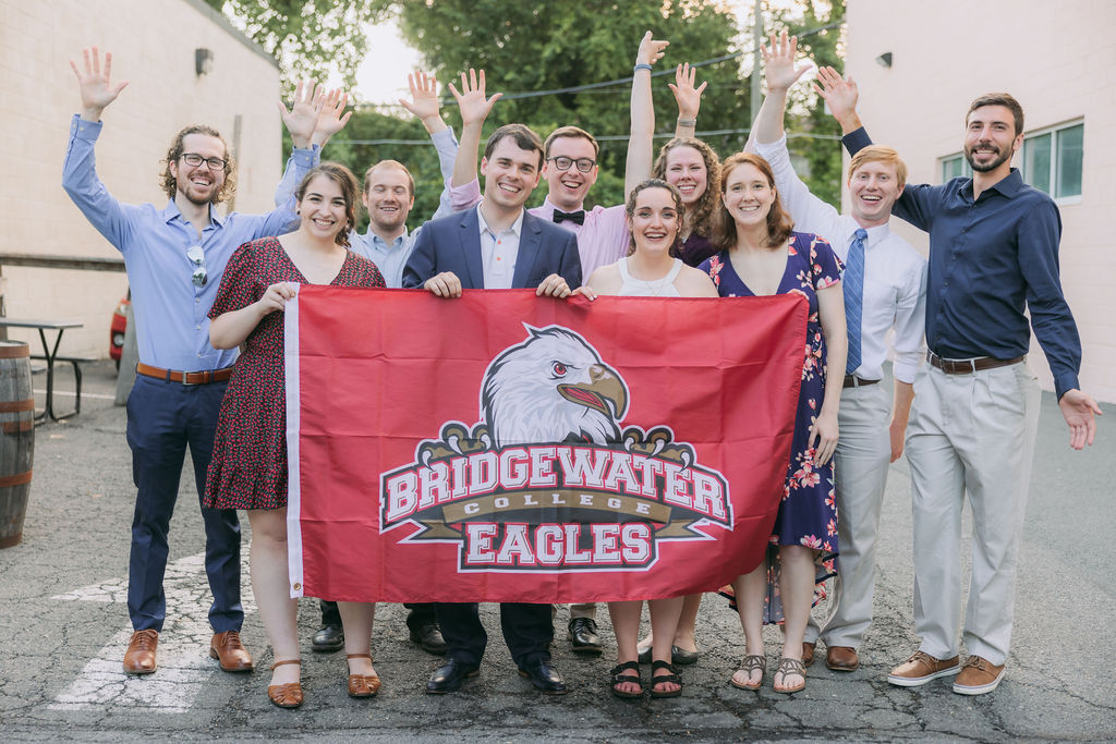 Group photo from a wedding with people looking excited and holding Bridgewater Eagles banner