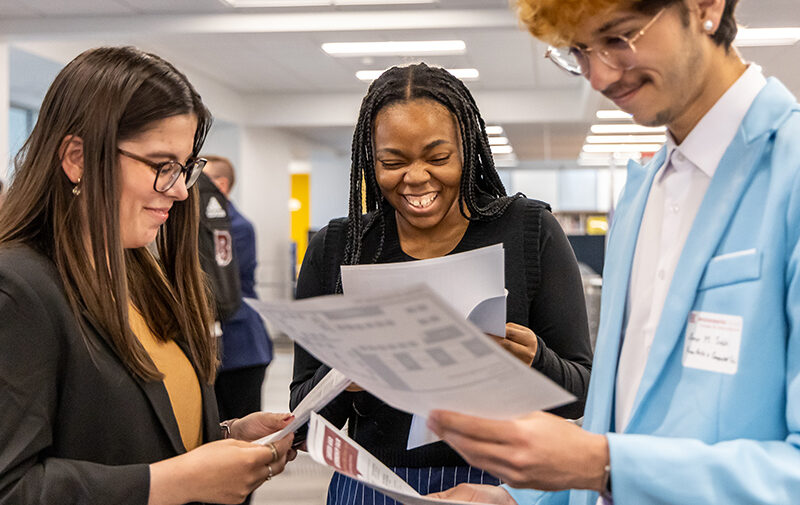 Three students gathered together with papers in hand