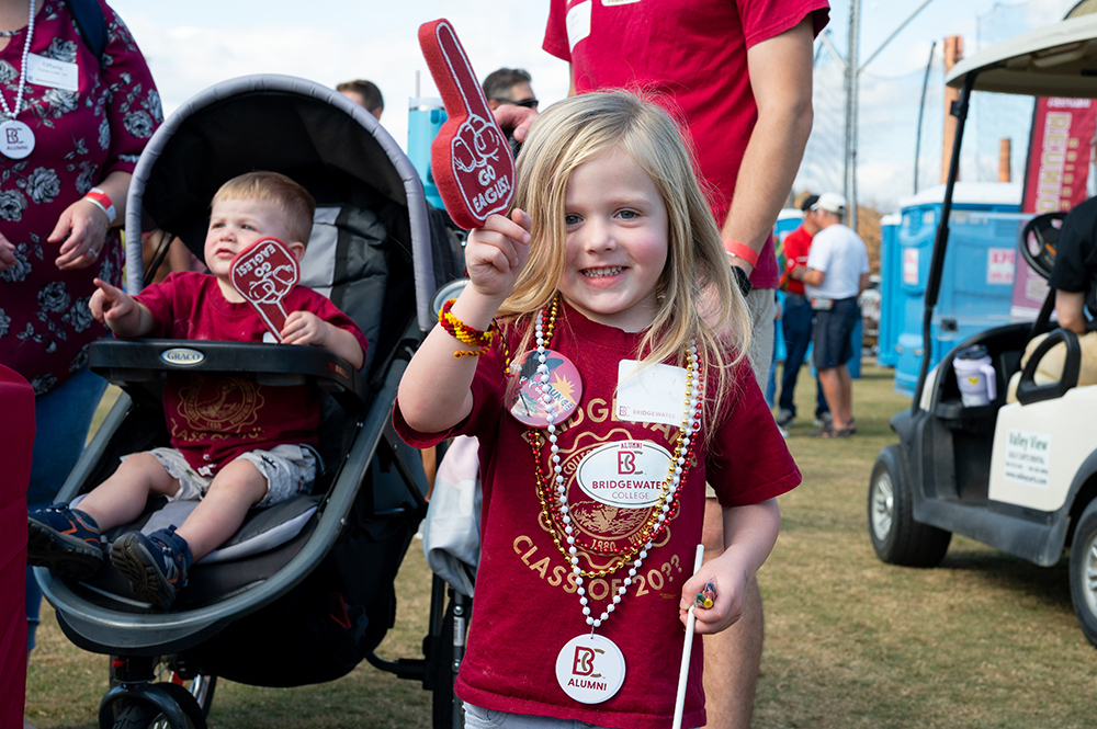 Little girl in the foreground holding up a little Go Eagles foam finger with young boy in a stroller in the background