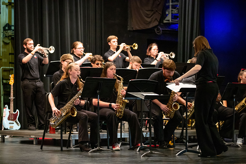 female conductor in front of band with mostly brass instruments