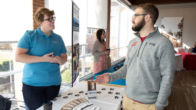 Non-profit Management graduate degree feature image - Two people talking at a fair with information about the R-H S-P-C-A