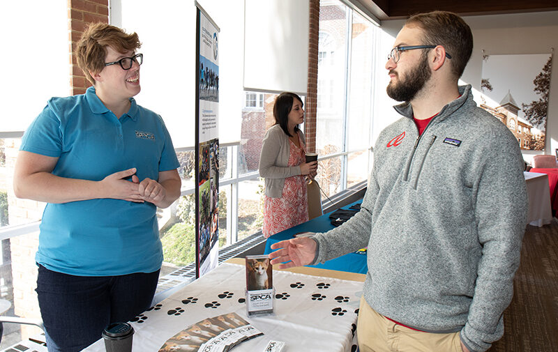 Non-profit Management graduate degree feature image - Two people talking at a fair with information about the R-H S-P-C-A