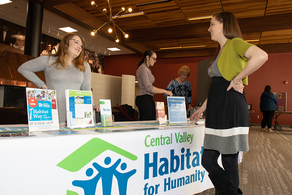 Two people talking in front of table that says Habitat for Humanity