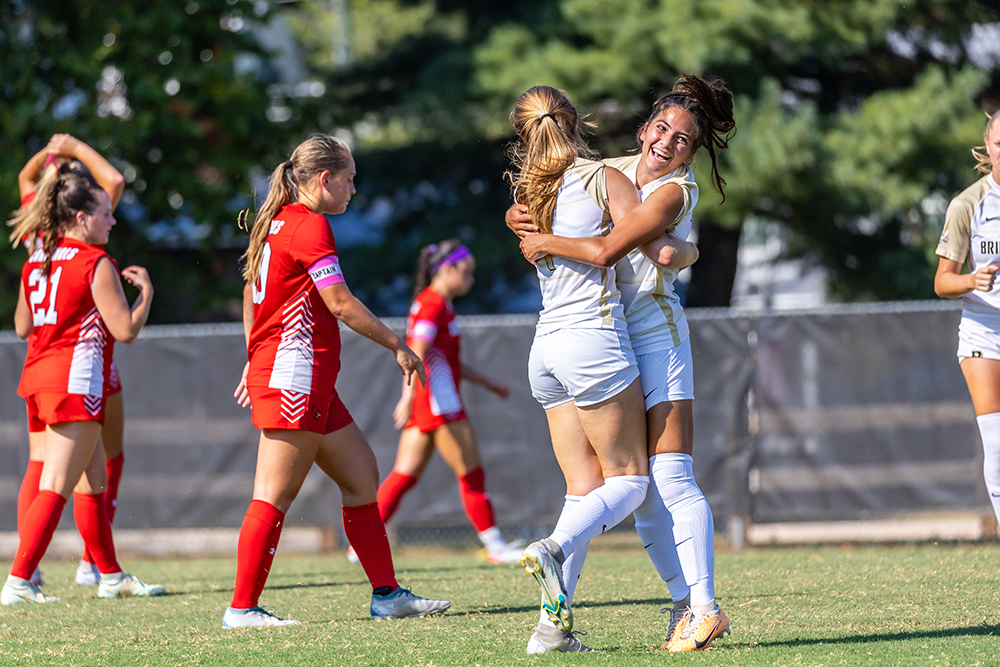 Two women's soccer players jumping up and hugging 