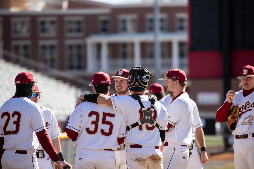 Bridgewater baseball team gathered at the pitchers mound. One player has his arm around the other. 