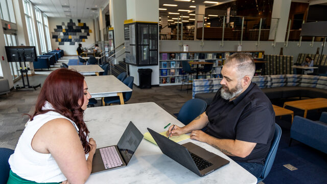 Professor and student sitting at a table each with a laptop