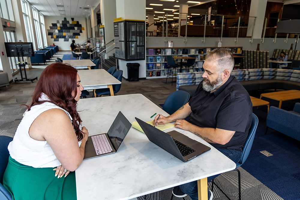 Professor and student sitting at a table each with a laptop