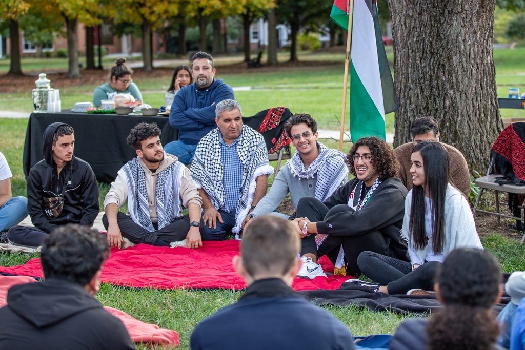 Students sitting on the ground in a half circle talking and smiling 