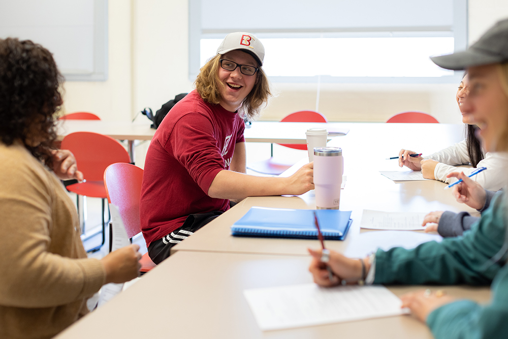 Student with B-C hat smiling among others at a table