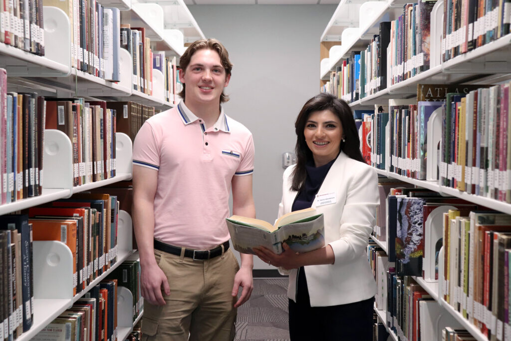 Jared Mullins and Dr. Sevinj Iskandarova standing between rows of books in the library