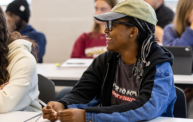 Student wearing a hat smiling in a sociology class