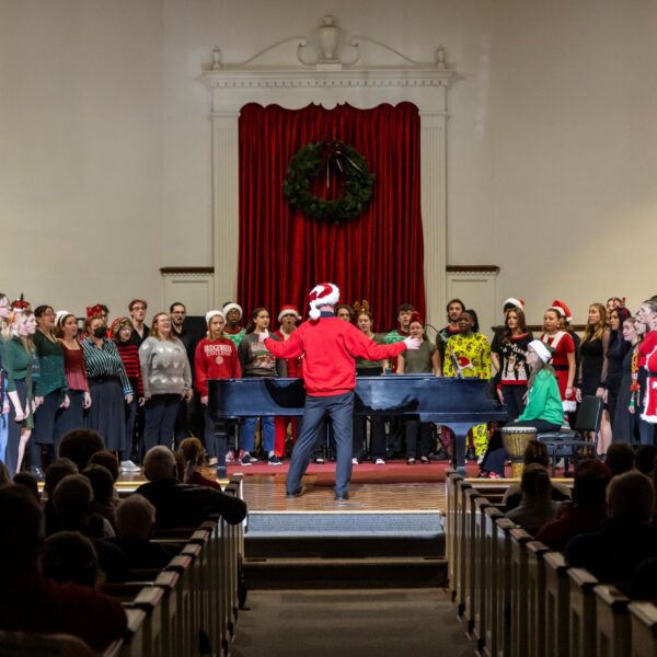 Choir singers dressed in holiday apparel perform on stage for an audience