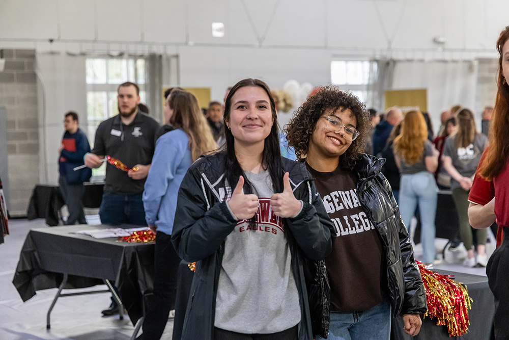 Two female students posing together and giving thumbs up to the camera