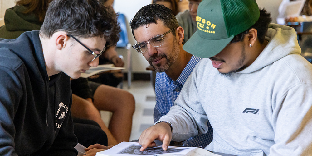 Professor meeting with two students as they look at a picture on the desk