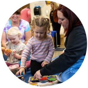 Student working with a little girl in a striped shirt on fitting shapes into a spot