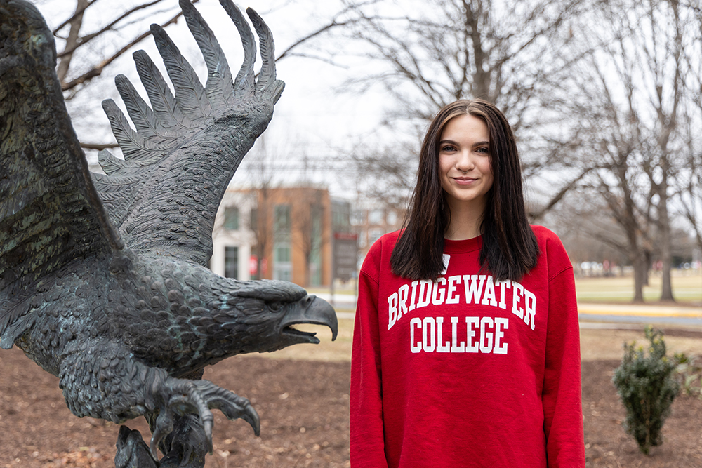 Kayla Stanley wearing crimson Bridgewater College sweatshirt standing next to Eagle statue