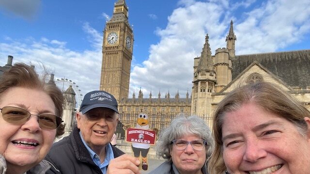 Four Bridgewater College alumni holding up Flat Ernie in front of Big Ben in London