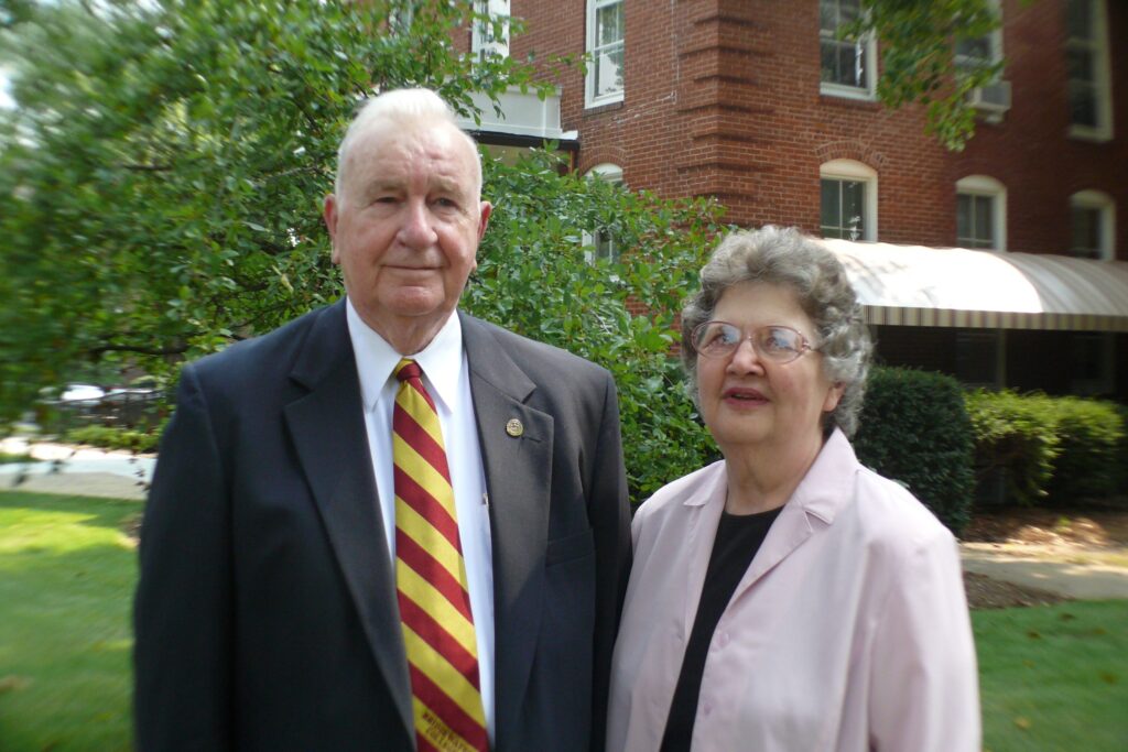 Marion E. Mason and his wife stand outside of Memorial hall by a tree