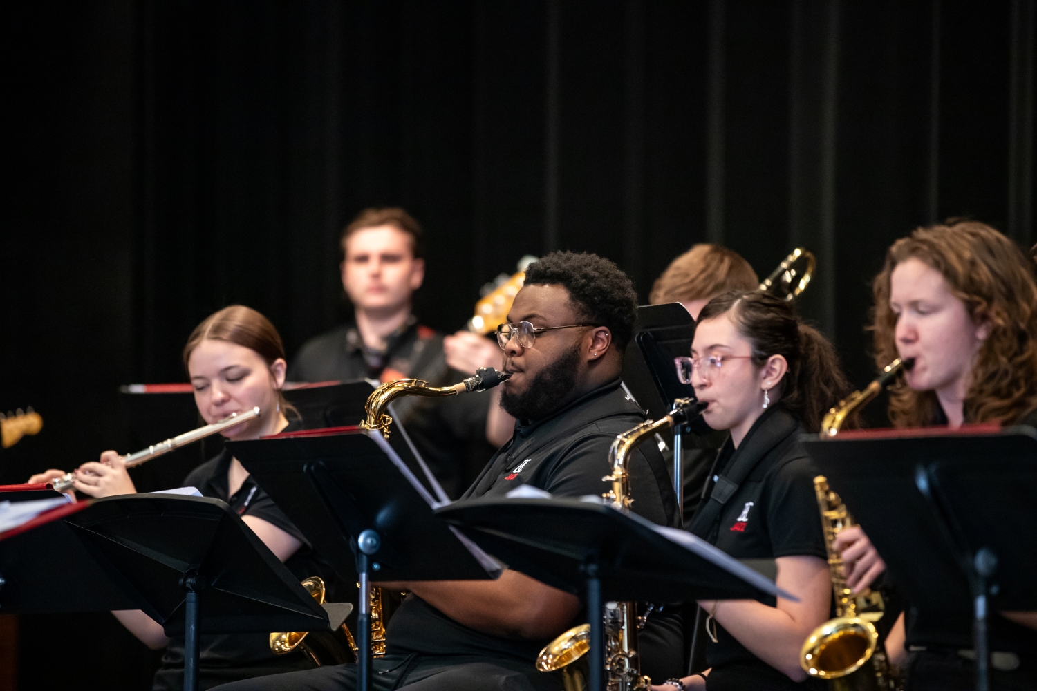 Three people sitting behind music stands playing saxophone